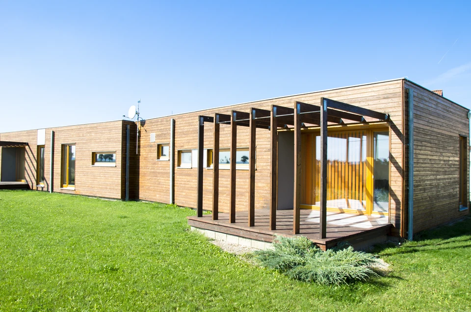 Maison modulaire moderne avec terrasse en bois, façade mixte bardage bois et panneaux blancs, toiture plate végétalisée