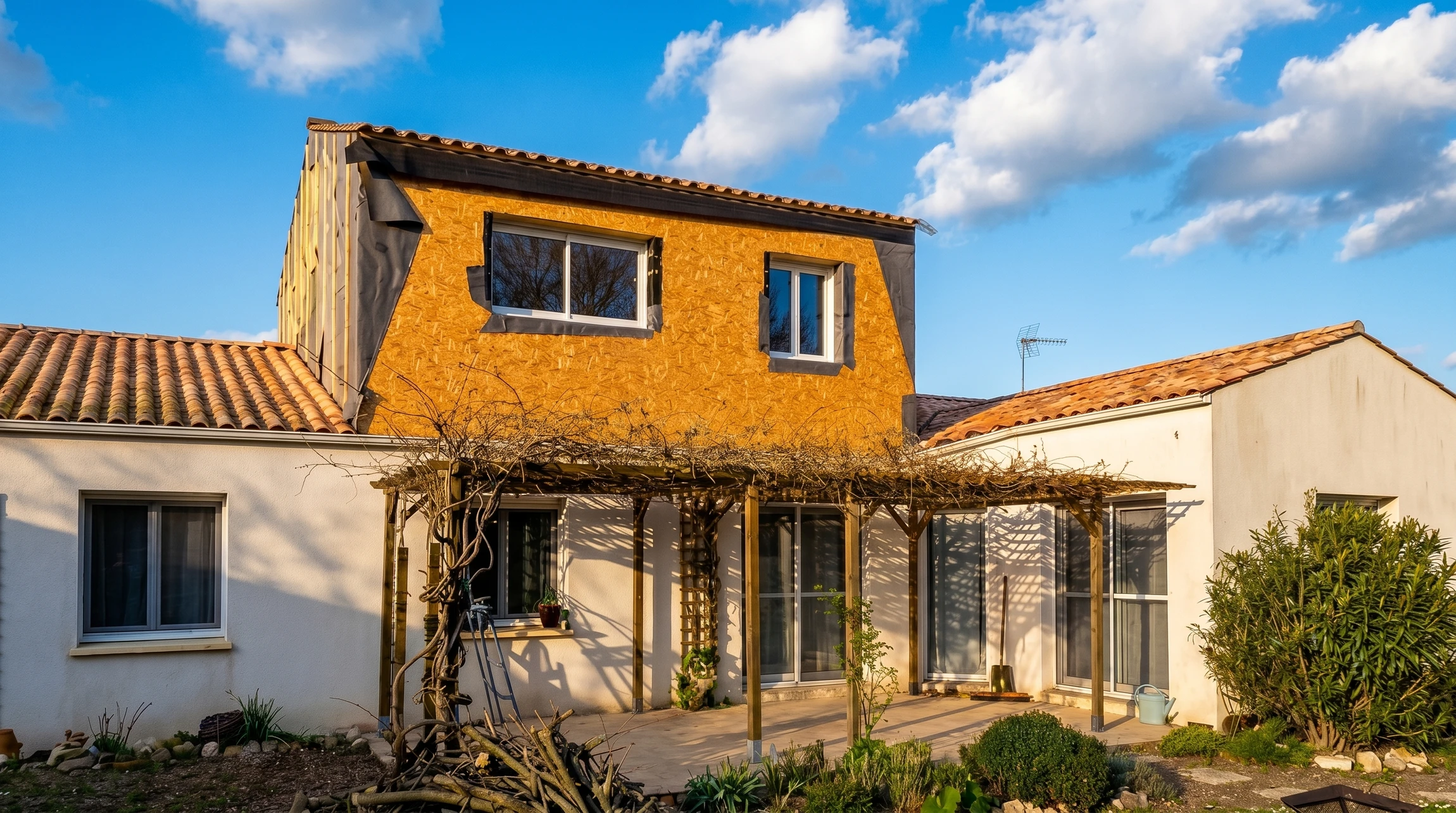 Maison contemporaine à deux niveaux avec façade mixte bois et crépi blanc, toiture métallique anthracite, baies vitrées illuminées