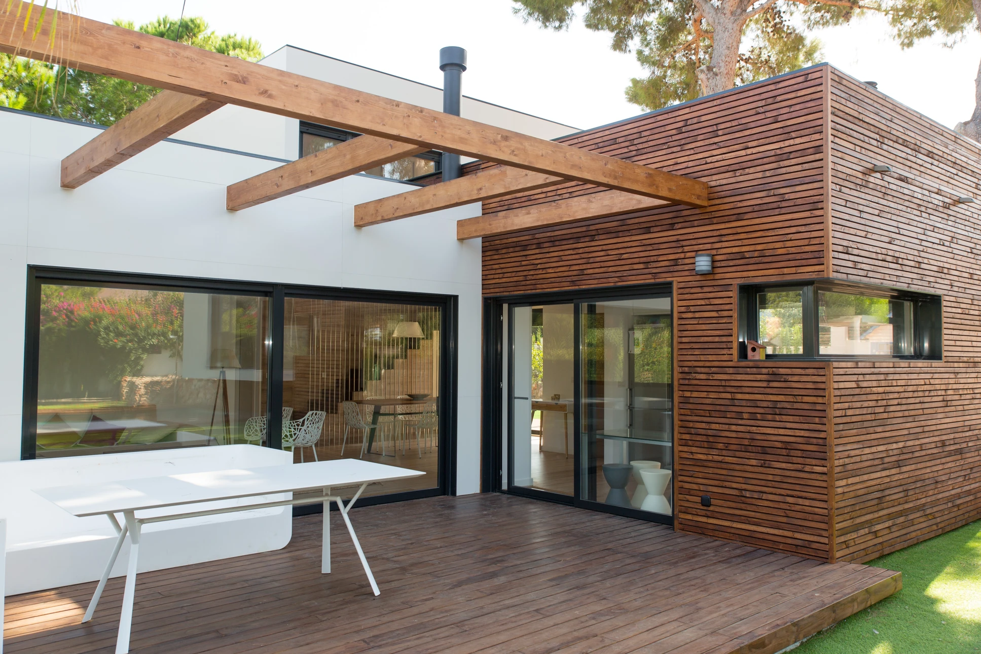Maison contemporaine en bois avec charpente apparente et large balcon, située dans un environnement verdoyant avec pelouse soignée et arbres matures