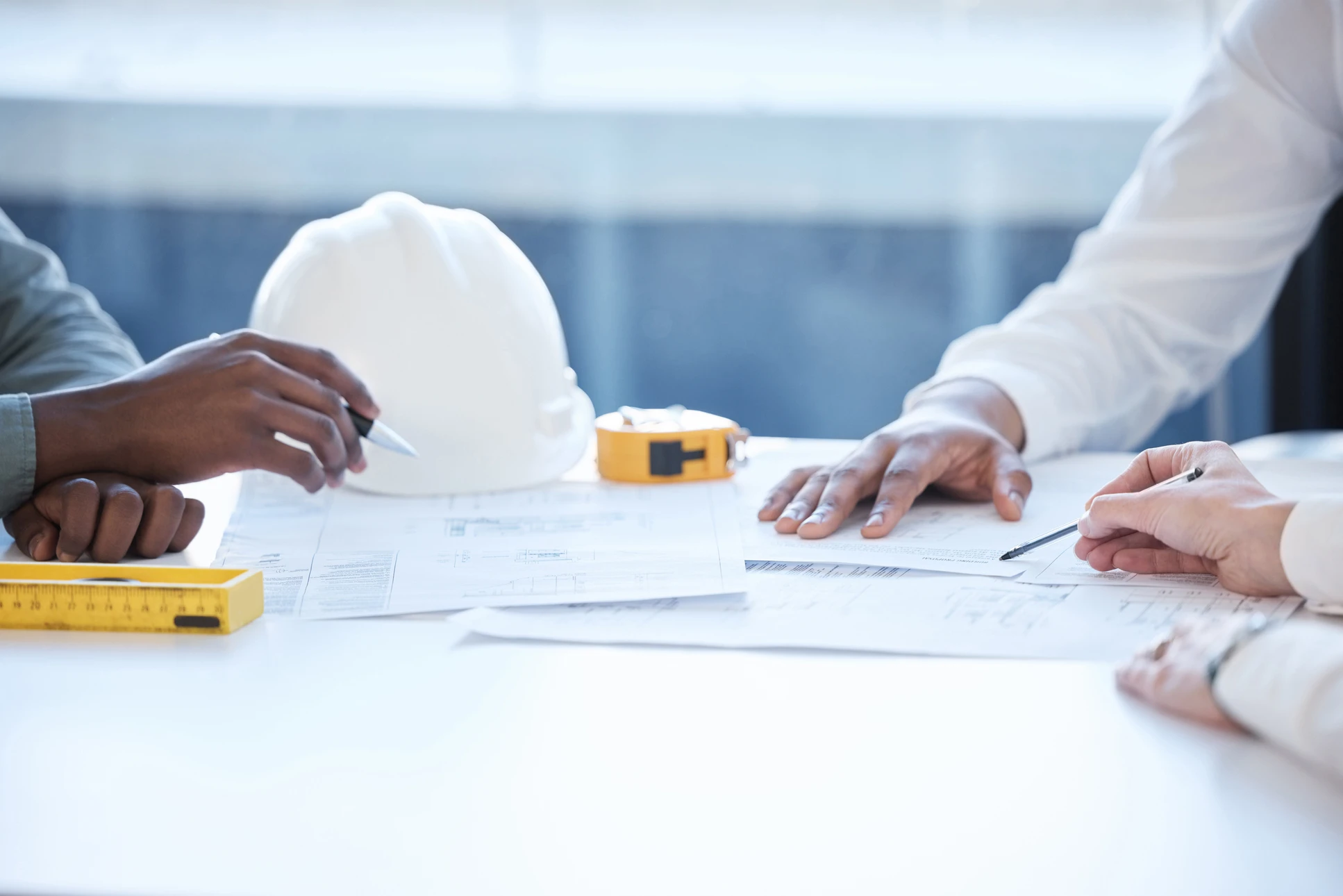 Deux professionnels examinent des plans architecturaux dans un bureau lumineux près d'une fenêtre